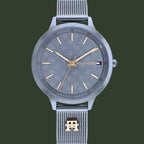 A Tommy Hilfiger men's analog watch with a silver-tone stainless steel case and mesh strap, featuring a textured gray dial with gold-tone hands and indices, and the brand's signature flag logo on the dial.