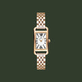 A women's rectangular quartz watch with a rose gold-tone metal case and link bracelet, featuring a white dial with black Roman numerals and gold hands.