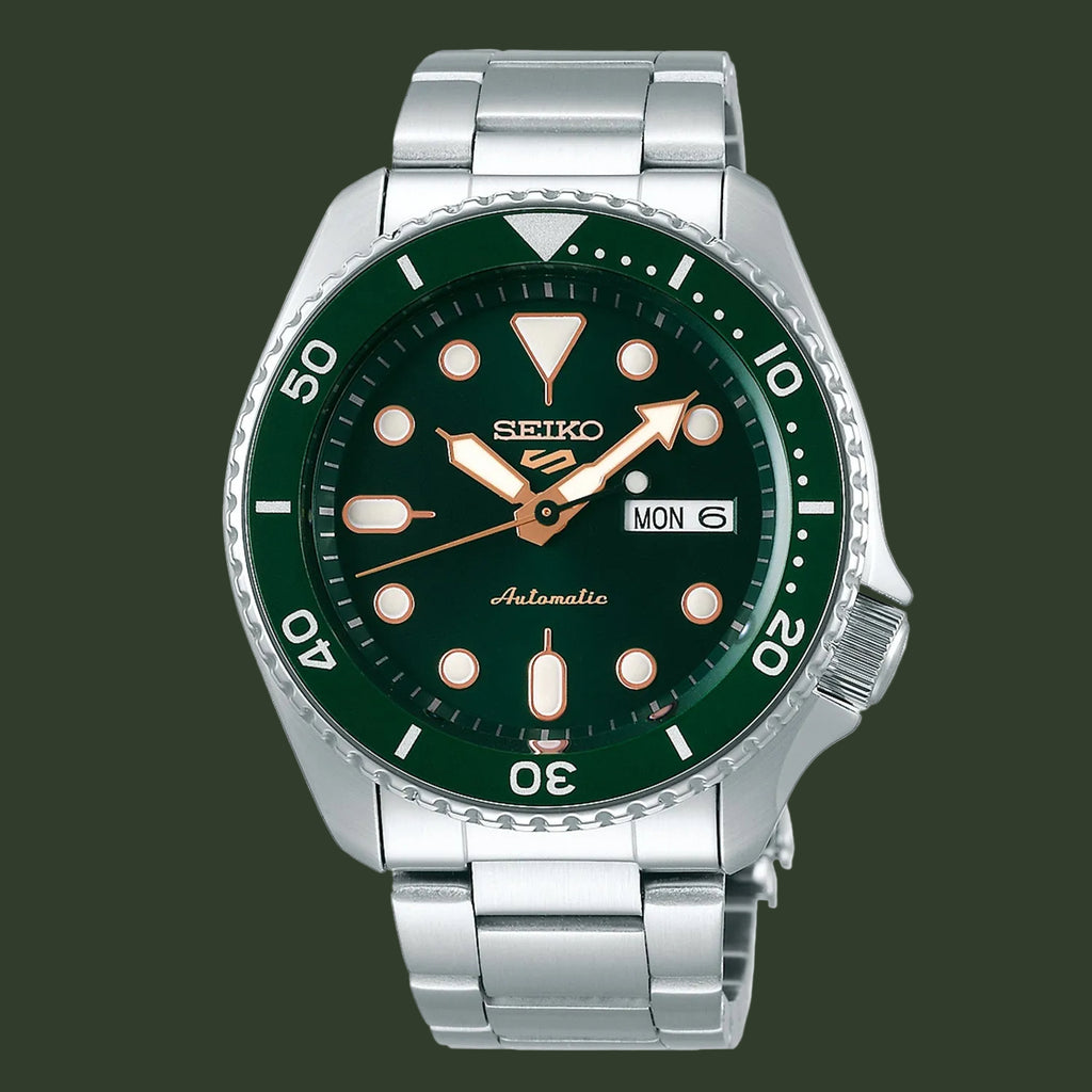 A Seiko automatic dive watch with a dark green dial and bezel, a silver stainless steel case and bracelet, and luminous orange hour markers.