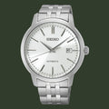 A Seiko automatic wristwatch with a silver stainless steel case and link bracelet, featuring a white dial with silver-tone hour markers and hands, and a date window at the 3 o'clock position.