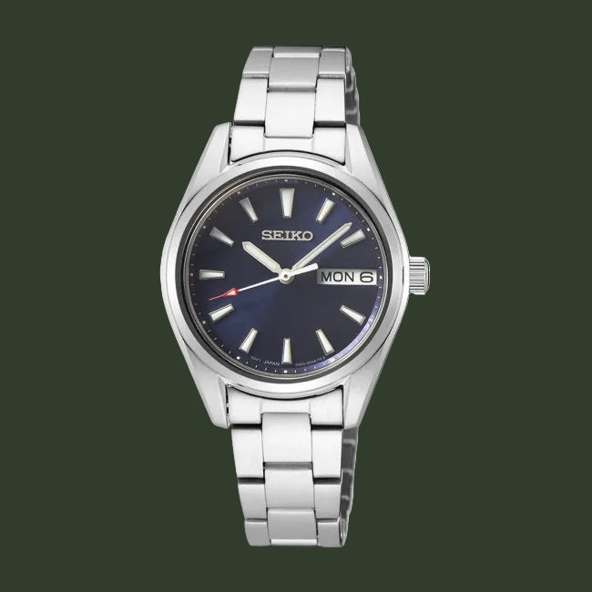 A Seiko women's analog watch with a silver stainless steel link bracelet, a silver case, and a dark blue dial featuring silver hour markers and hands, with a day and date window at 3 o'clock.