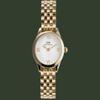 A Daniel Wellington DW001 women's watch featuring a gold-tone stainless steel case and link bracelet, a white dial with gold-tone Roman numerals and hands, and a crown on the right side of the case.