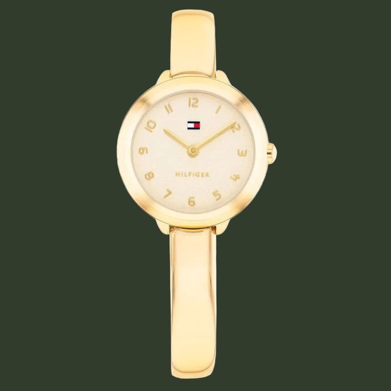A gold-tone Tommy Hilfiger bangle watch with a round bezel, cream-colored dial, and a matching gold bangle strap, shown against a plain white background.