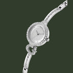 A silver-tone women's analog watch with a round crystal-studded bezel, matching crystal-embellished bracelet, and a textured white dial. The brand name 'GUESS' is visible on the dial.